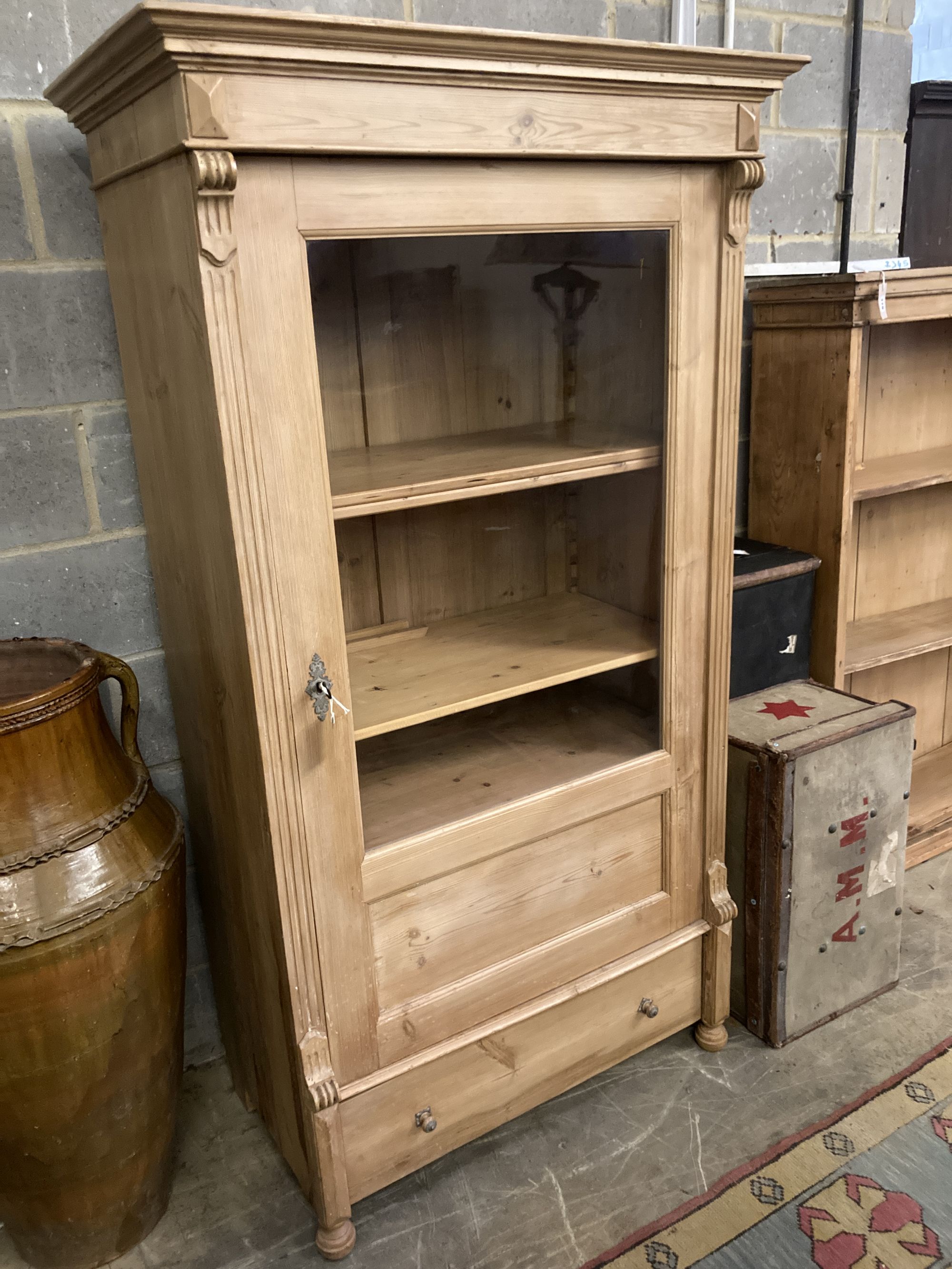 A pine display cabinet, fitted single glazed door enclosing four shelves over base drawer, width 100cm, depth 55cm, height 183cm